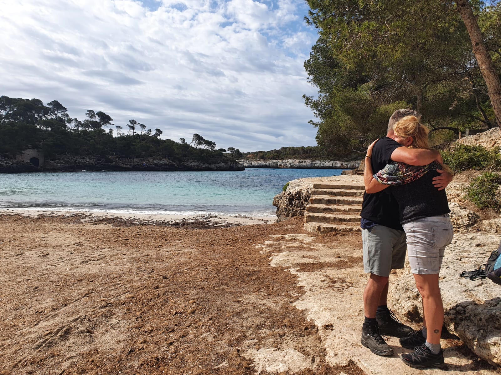 A couple standing arm in arm above a quiet Mallorcan cove