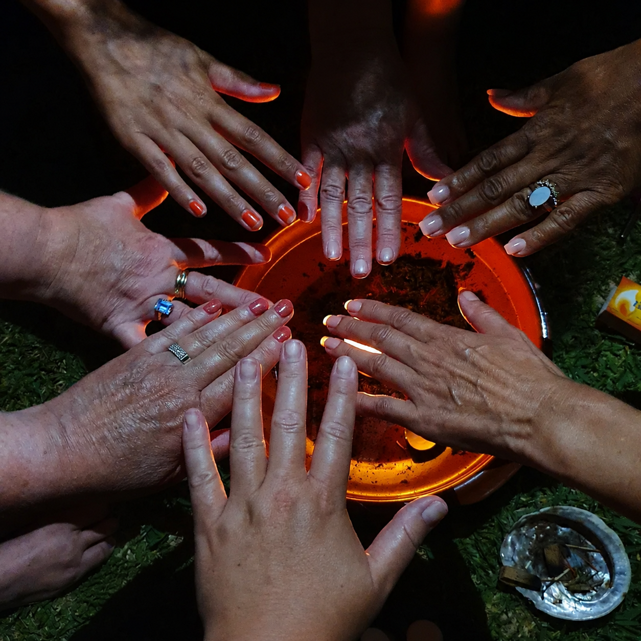 Hands gathered around a glowing fire bowl during an evening ritual